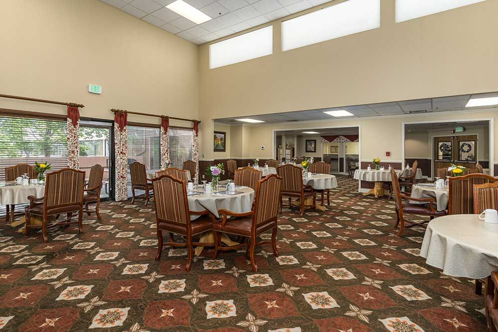 A spacious dining room with neatly arranged tables and chairs, featuring a decorative carpet and ample natural lighting.