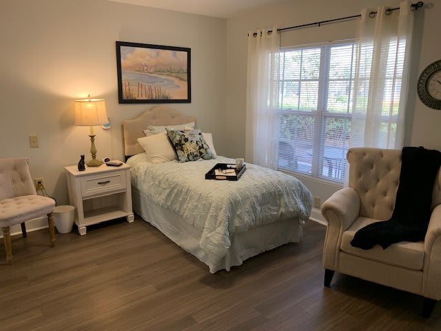 A cozy bedroom with a single bed, nightstand, and armchair by the window.