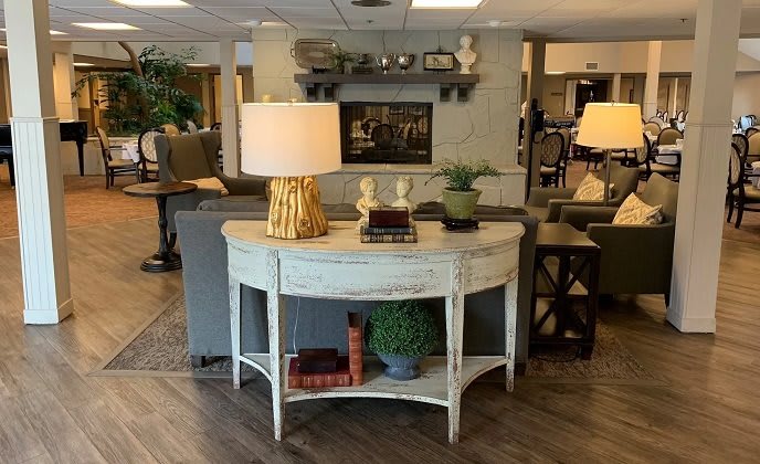 A cozy living room setup featuring a distressed console table with a lamp, books, and decorative plants.