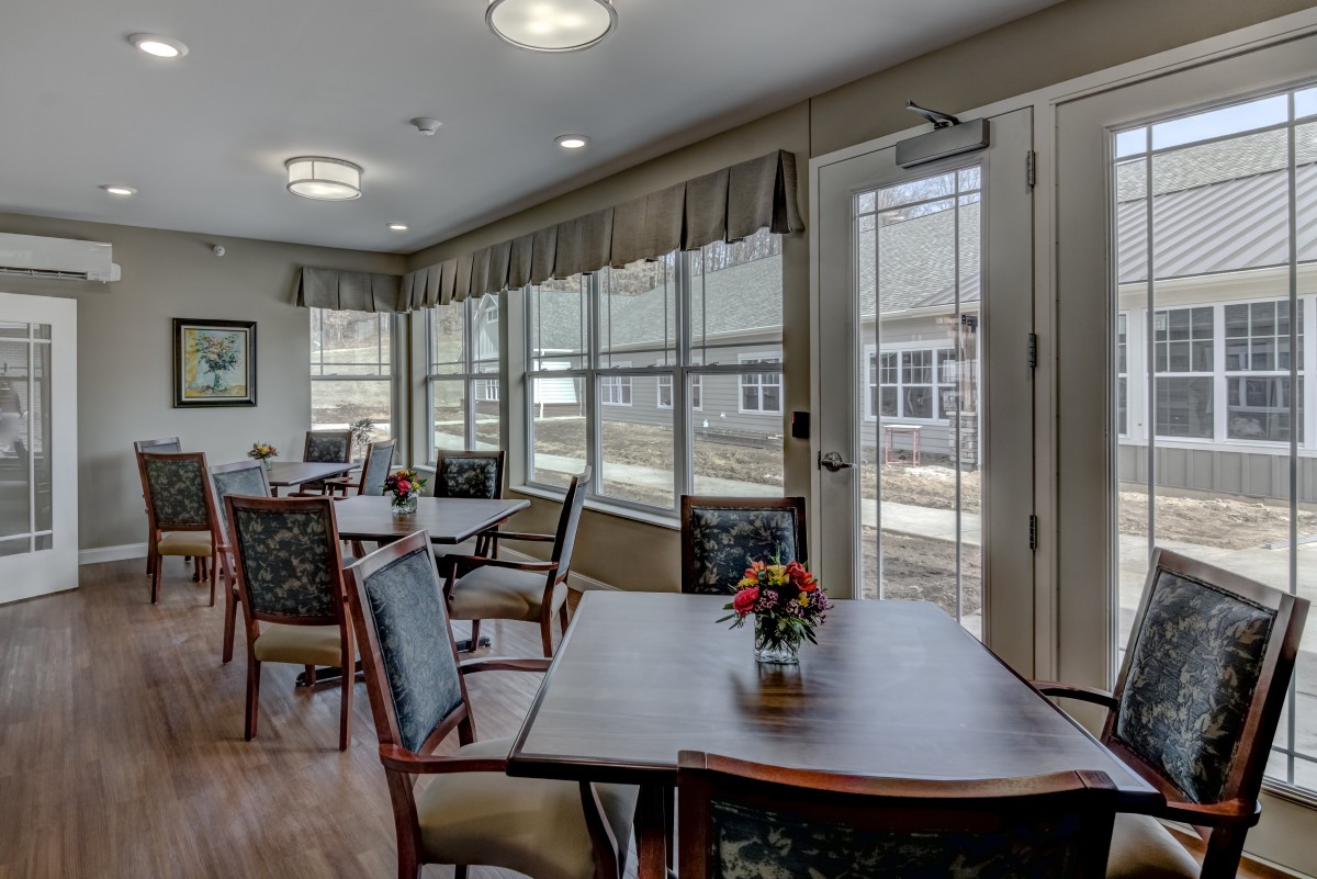 A well-lit dining area with tables and chairs arranged near large windows.