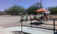 A sunny patio with seating and an orange umbrella.