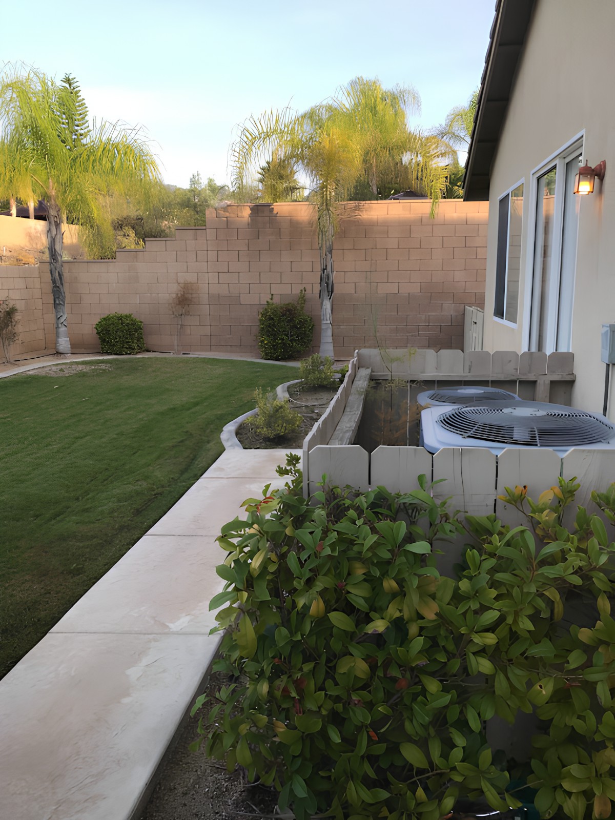 A neatly landscaped backyard with a patio and green lawn surrounded by plants and a privacy fence.