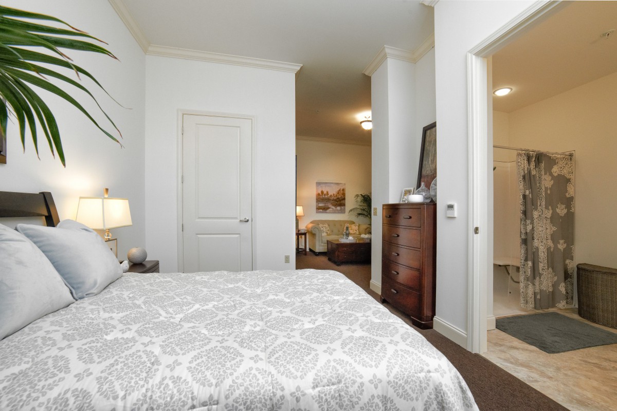 A modern bedroom with a bed, dresser, and an adjoining bathroom.