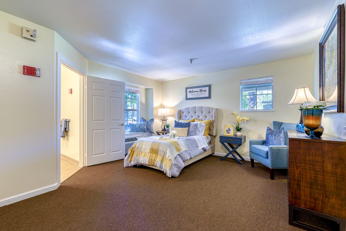 A cozy and well-decorated bedroom featuring a bed with patterned bedding, a lamp, and comfortable seating.