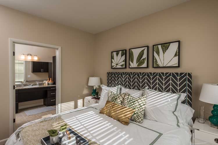 A modern bedroom with stylish decor, featuring botanical artwork and patterned pillows.