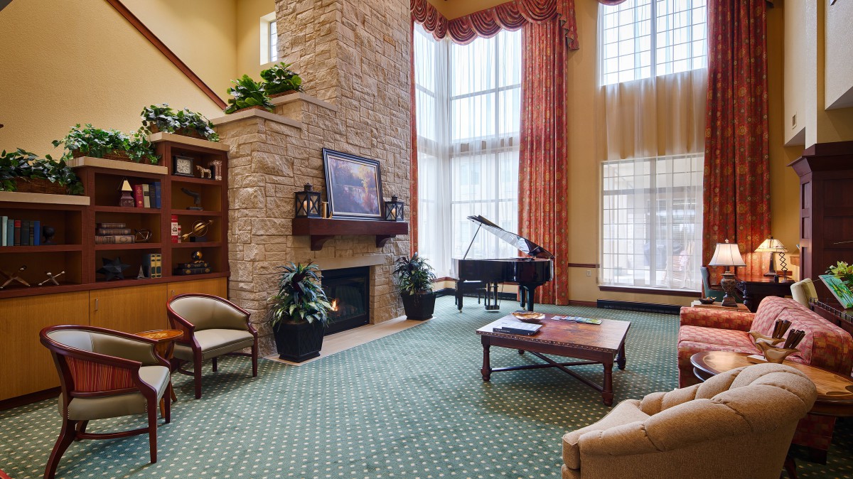 A spacious living room with a grand piano, stone fireplace, and tall windows.