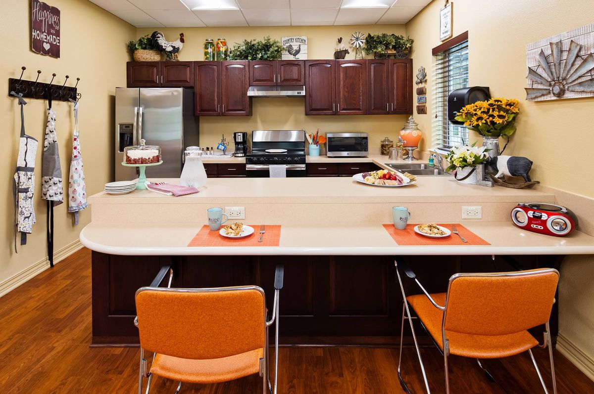 A modern kitchen with stainless steel appliances and orange chairs at the countertop dining area.