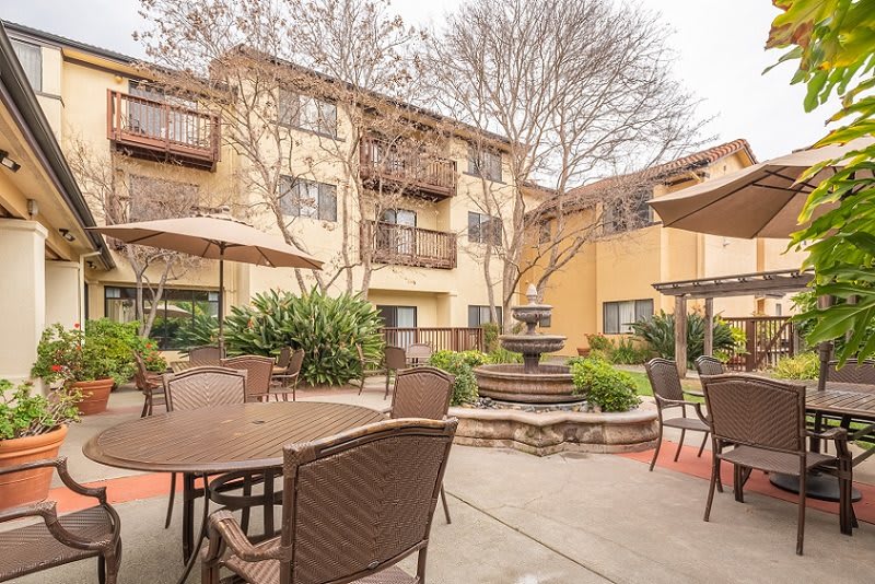 A cozy courtyard of an apartment building with outdoor seating and a central fountain, surrounded by trees.