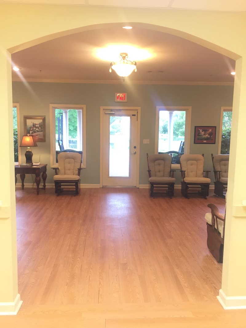 A cozy waiting room with a wooden floor and several chairs arranged along the walls.