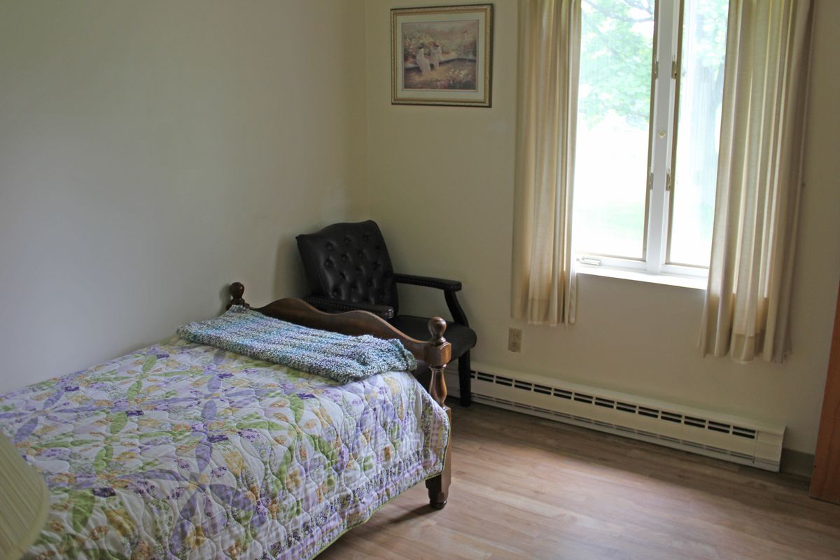 A simple bedroom with a single bed, chair, and window with curtains.