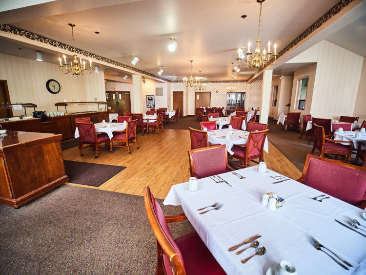 A spacious restaurant dining area with neatly arranged tables and chairs, adorned with chandeliers and white tablecloths.