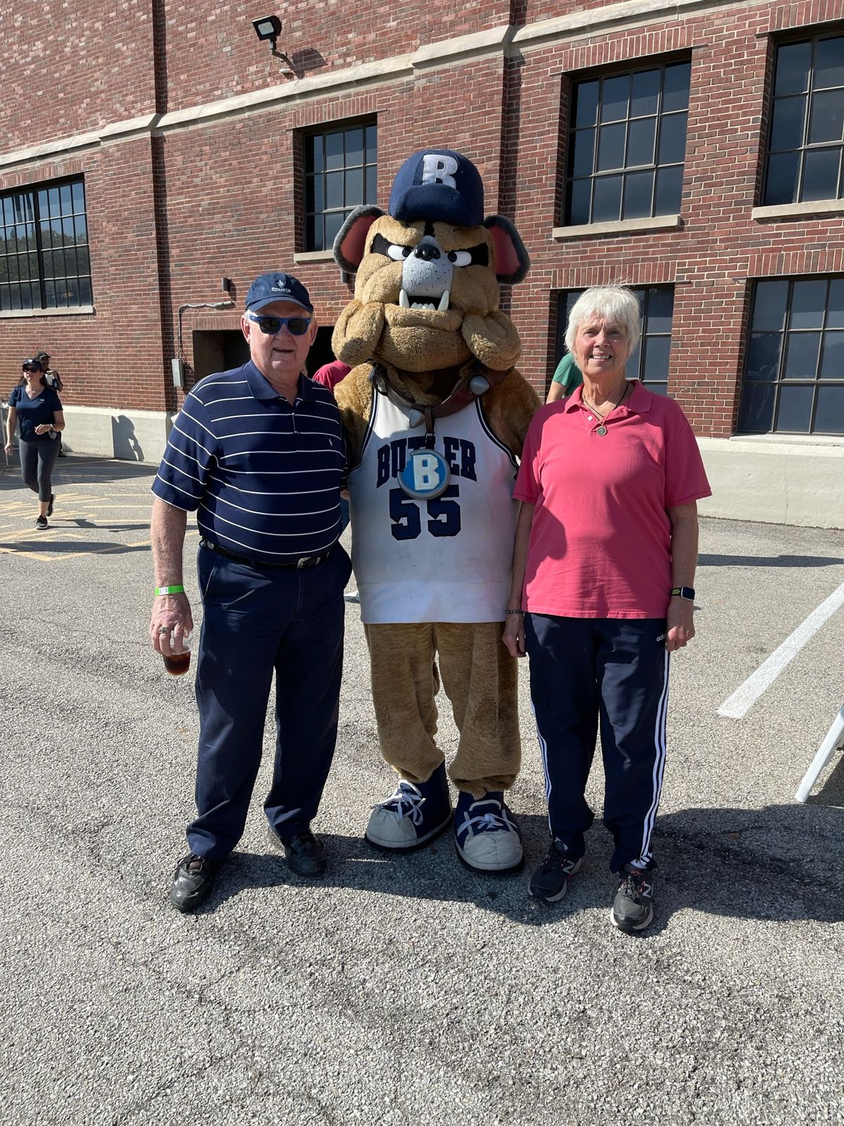 A couple poses with a sports mascot outside on a sunny day.