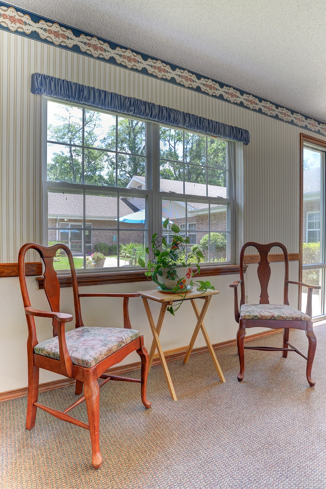 A cozy sitting area with two wooden chairs and a small table holding a plant by the window.