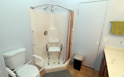 An accessible bathroom featuring a shower with a safety chair and rail.