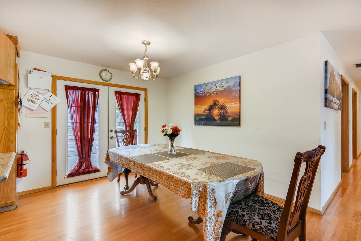 A cozy dining room with a table set for two, adorned with a floral arrangement and an elegant chandelier overhead.