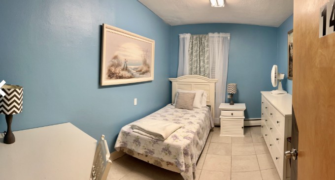 A cozy bedroom with blue walls, featuring a single bed, a nightstand, and a decorative painting.