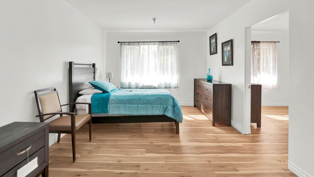 A modern, minimalist bedroom with wooden flooring and natural light.
