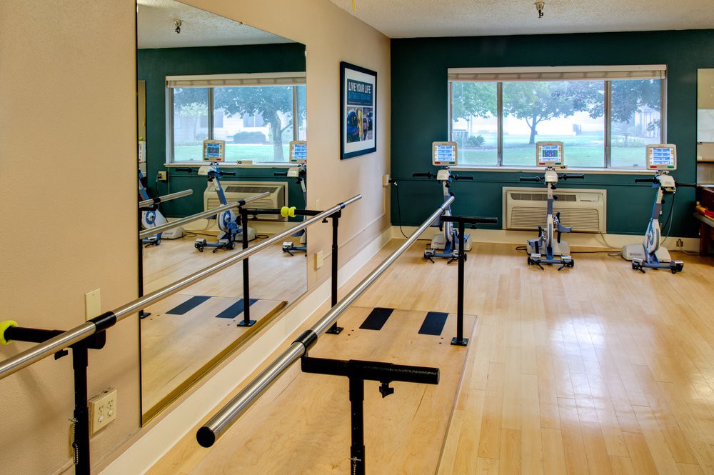A well-equipped exercise room featuring a ballet barre, mirrors, and stationary bikes with large windows providing plenty of natural light.