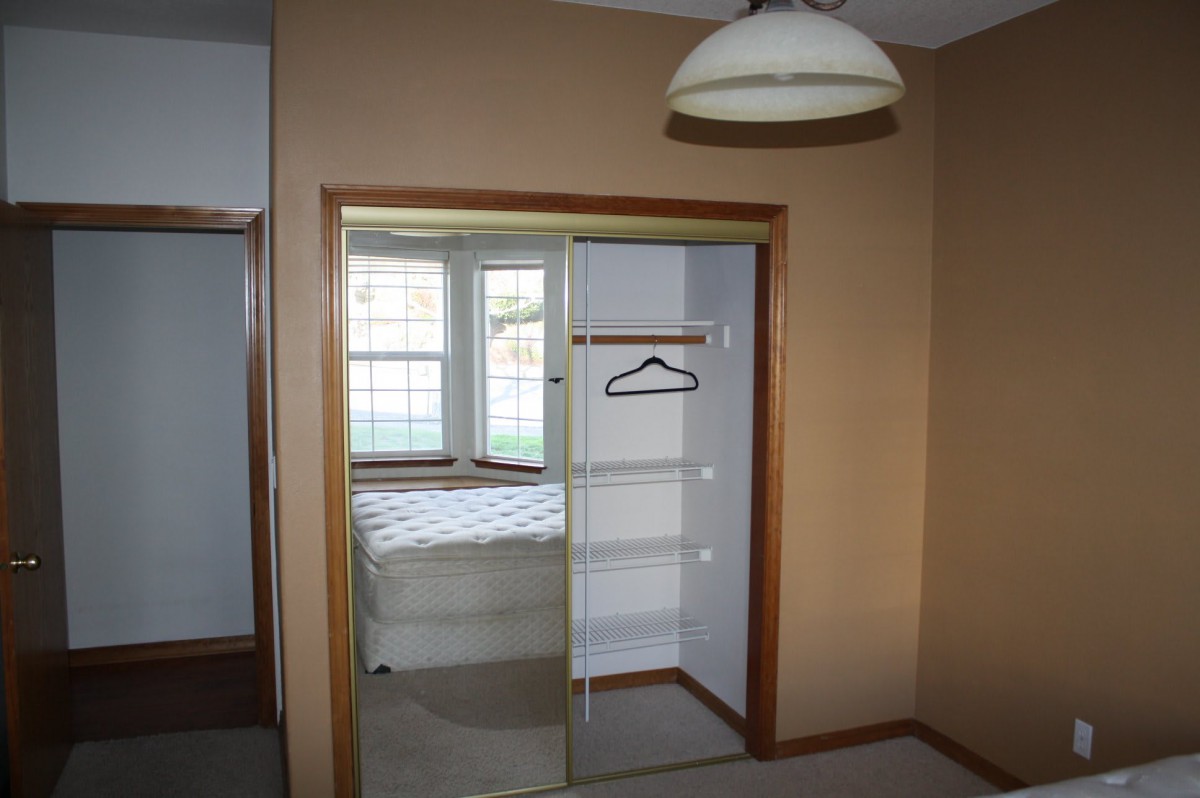 A bedroom with a mirrored closet door and a window.