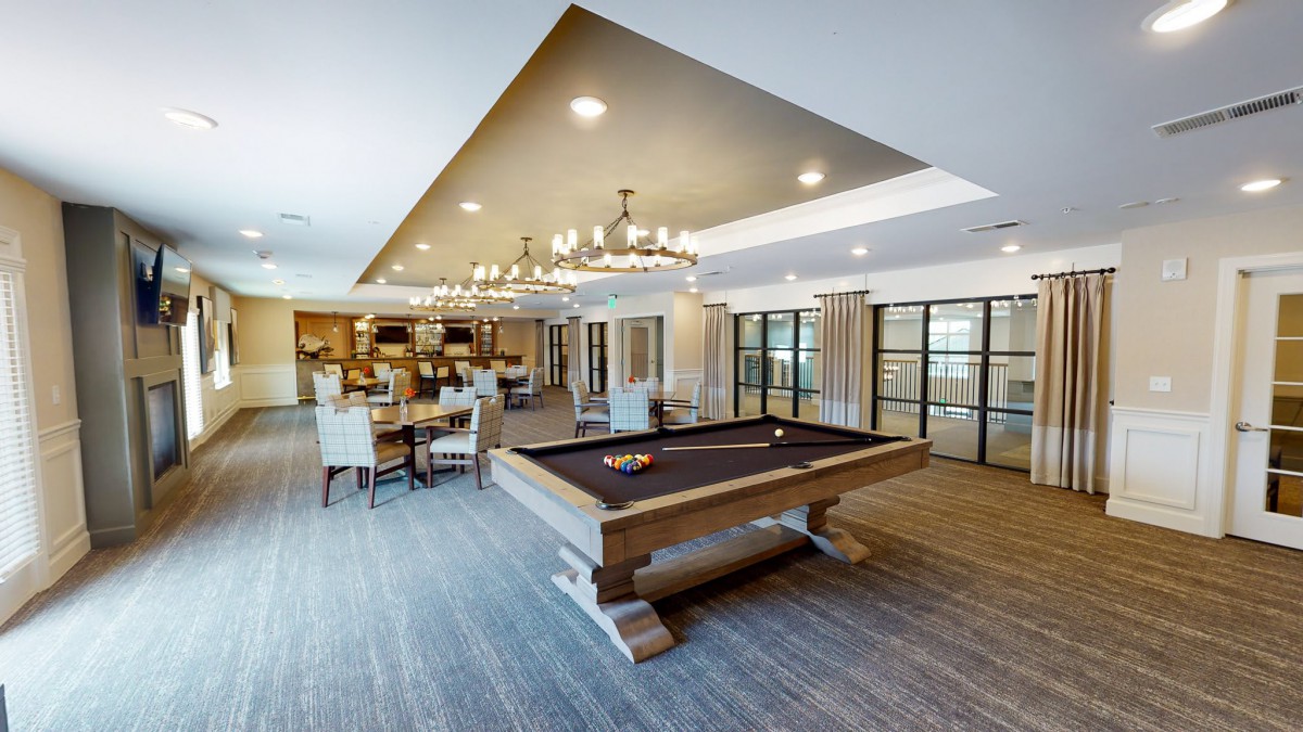 A modern game room featuring a billiard table and elegant seating area with chandeliers.