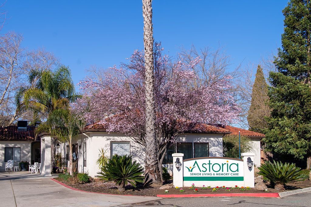 A small building with a 'Astoria' sign surrounded by blooming trees and palm.