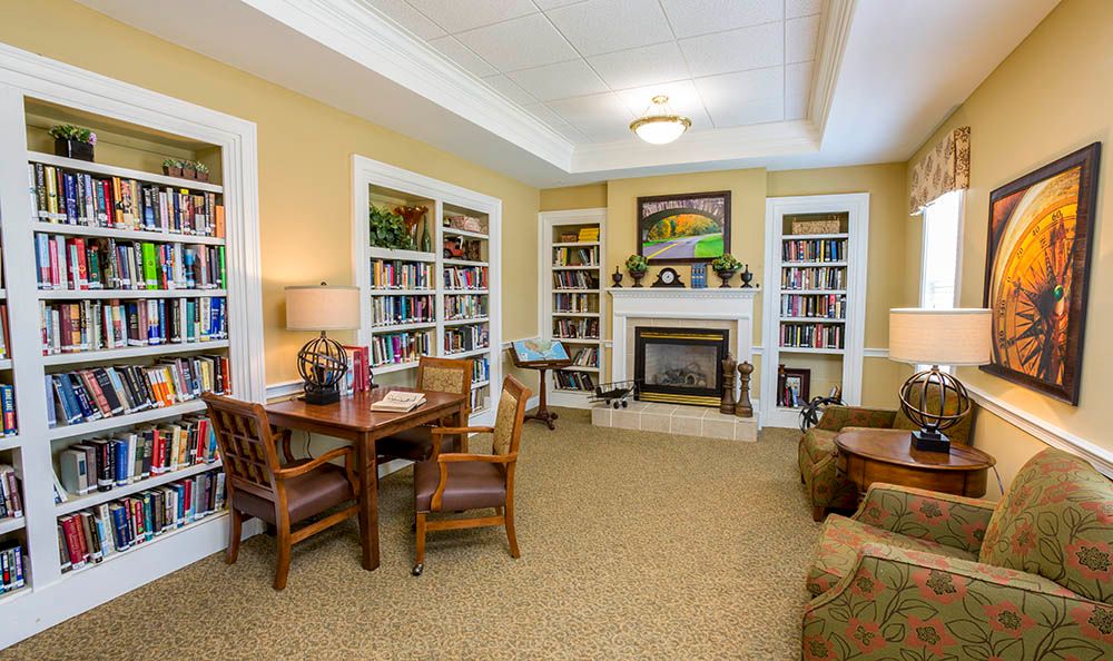 A cozy living room with bookshelves and a fireplace, featuring a table and chairs for lounging.