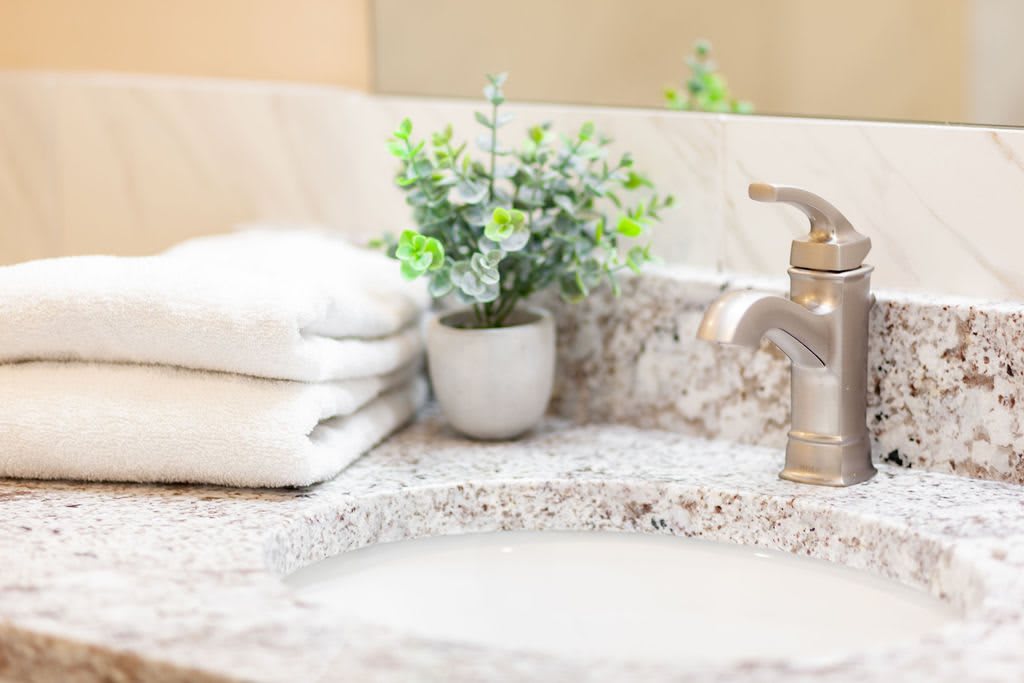 A clean and tidy bathroom sink with a granite countertop, neatly folded towels, and a small potted plant for decoration.