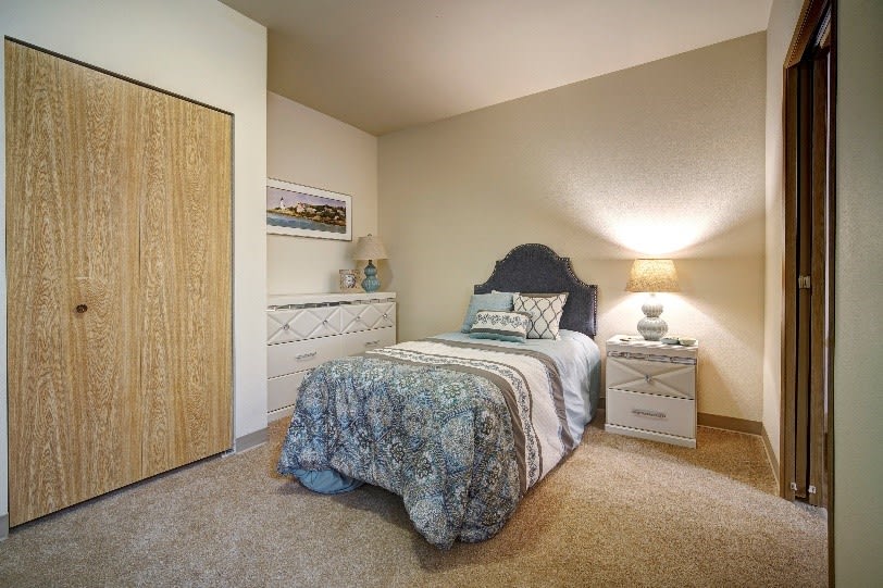 A cozy bedroom with a single bed, nightstand, and dresser in neutral tones.