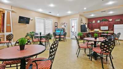 A well-lit dining area with multiple tables and chairs, decorated with plants and a television mounted on the wall.