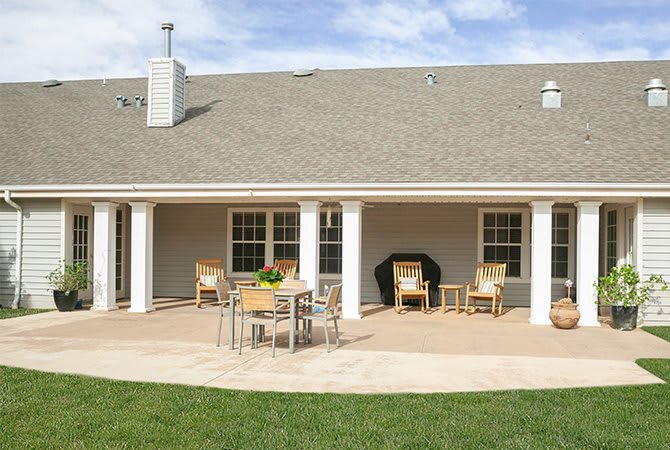 A backyard patio with outdoor furniture, including a table and chairs, set against a brick house with columns.