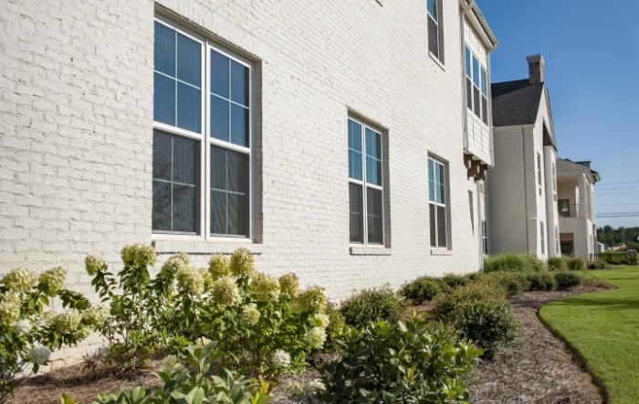 A side view of a brick house with windows and a landscaped garden on a sunny day.