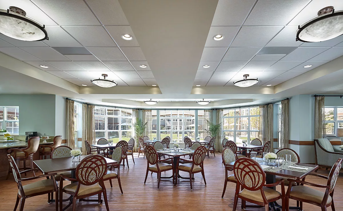 A spacious dining area with multiple tables and chairs, featuring large windows that allow natural light to pour in.