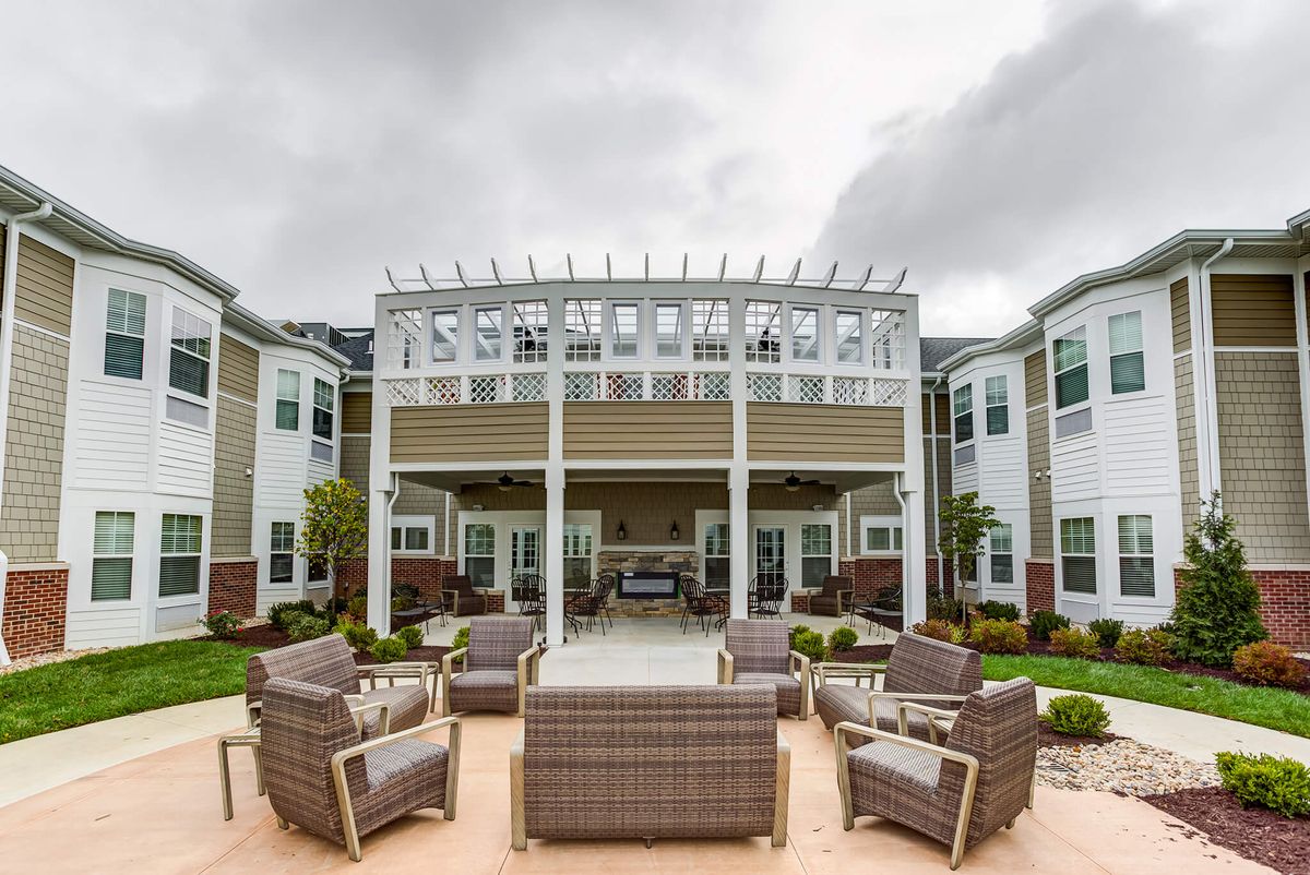 An outdoor patio area featuring comfortable seating under a pergola, surrounded by a well-maintained building and landscaping.