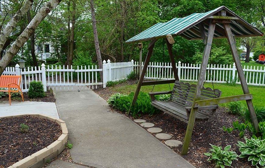 A peaceful garden scene with a wooden swing and a white picket fence.