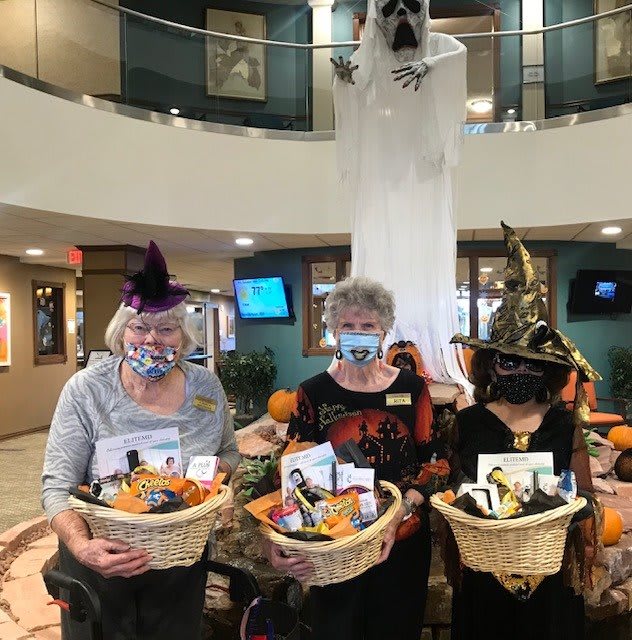 Three people in Halloween costumes holding themed baskets indoors.