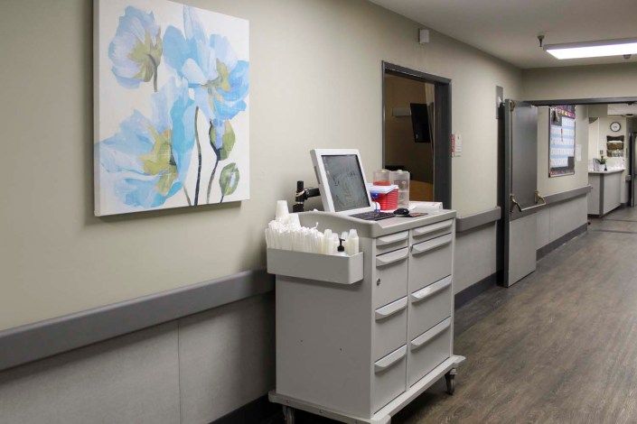 A hospital hallway featuring a medical cart and a floral painting on the wall.