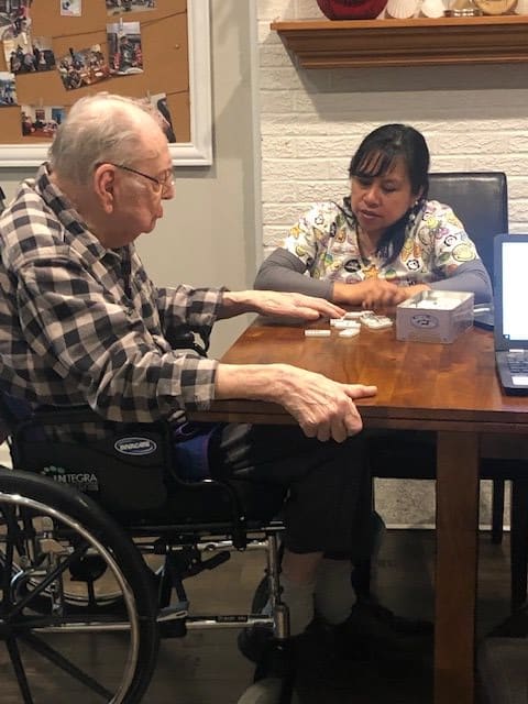 An elderly man in a wheelchair consulting with a healthcare worker at a table.