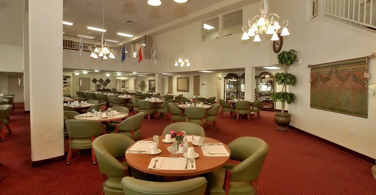 An elegant restaurant interior with neatly arranged tables and chairs, featuring classic lighting fixtures and a carpeted floor.