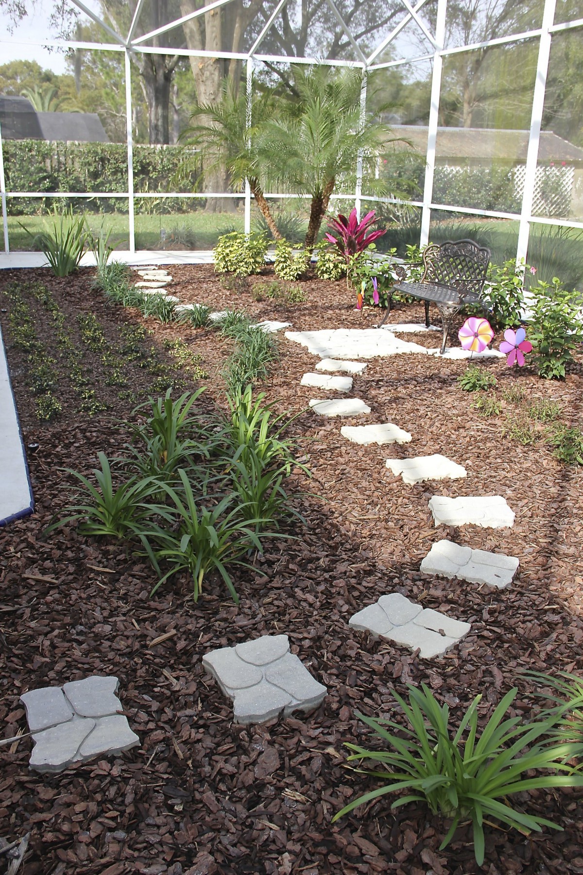 A garden with a curvy pathway made of stepping stones surrounded by mulch and greenery.