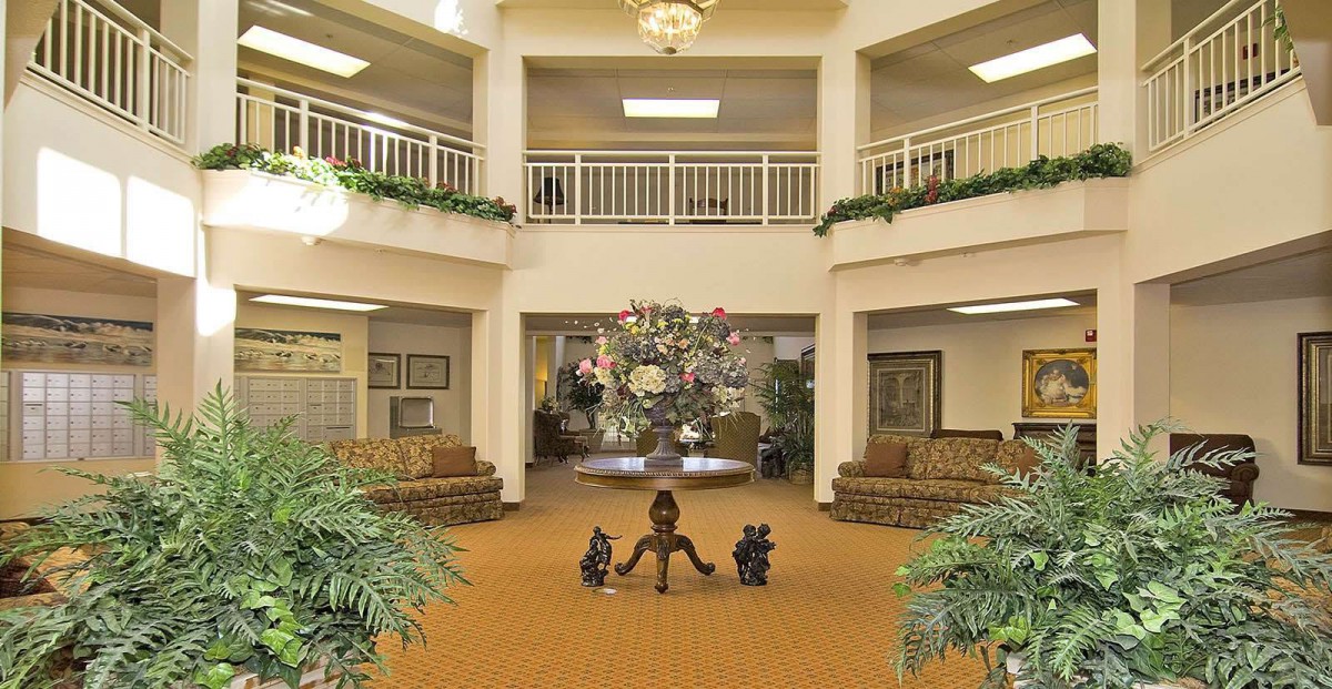 A spacious lobby with elegant decor, featuring comfortable seating, greenery, and a central chandelier.