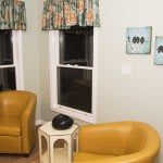 A cozy living room corner featuring yellow chairs, colorful curtains, and small artworks on the wall.