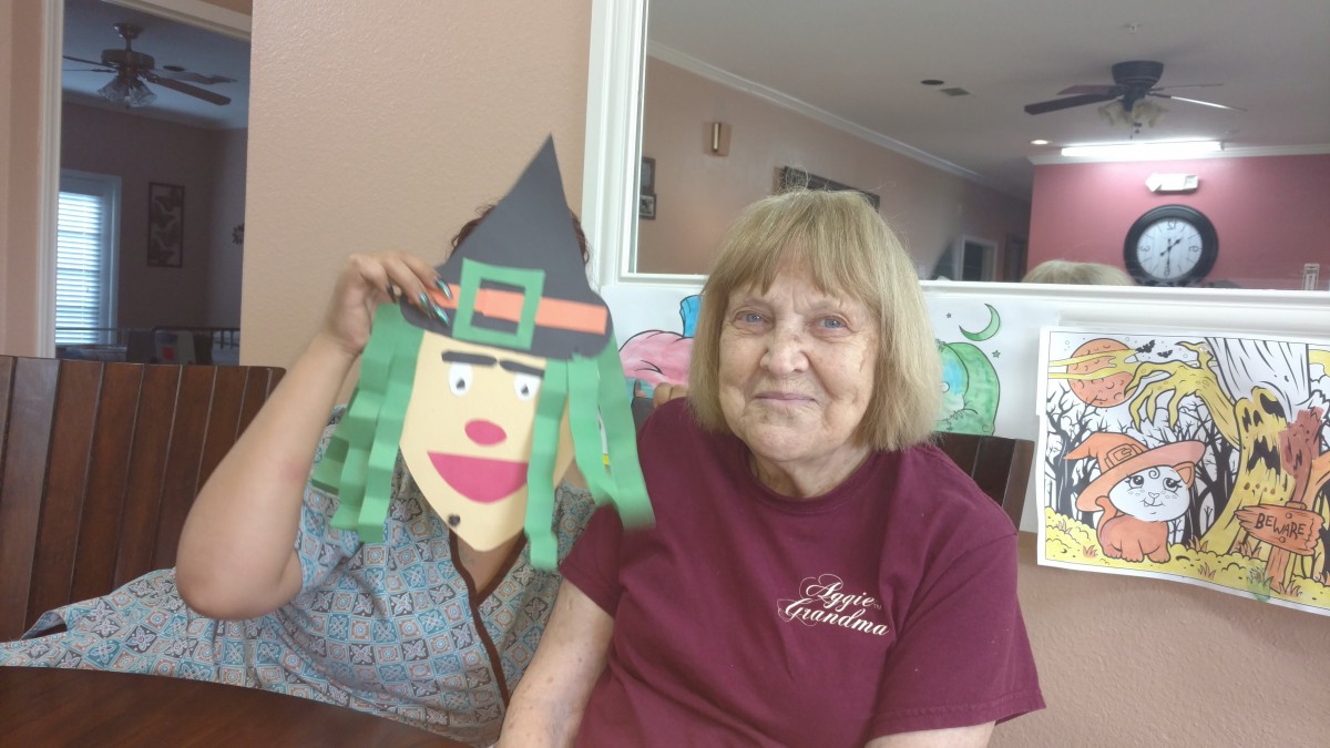 A woman smiles next to a paper witch craft indoors.