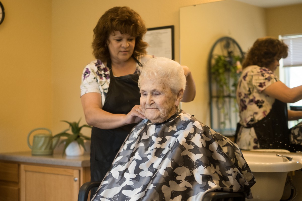 A hairstylist cutting an elderly woman's hair in a salon.