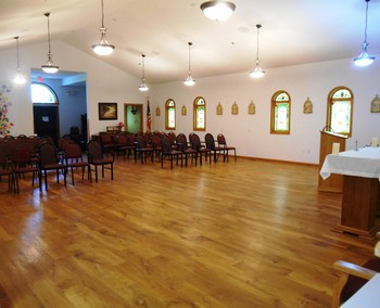 An empty chapel room with wooden floors and rows of chairs.
