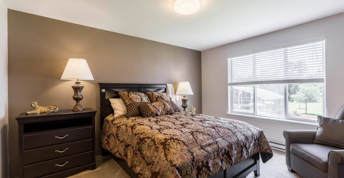 A cozy bedroom with a neatly made bed, bedside lamps, and a large window.