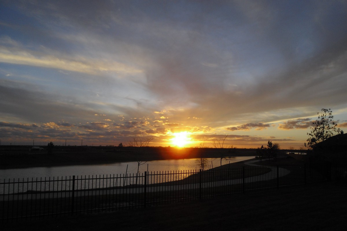 A serene sunset over a river with a silhouetted fence in the foreground.