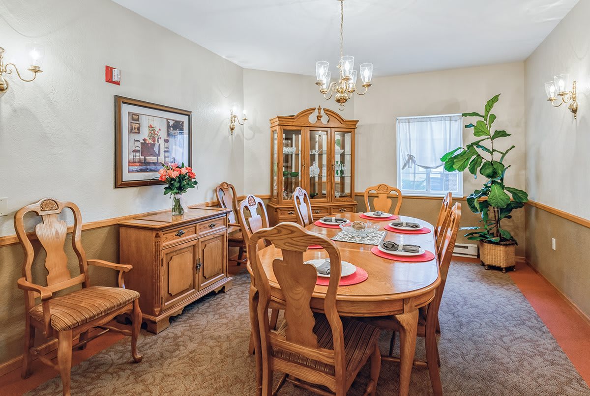 A cozy dining room with wooden furniture, featuring a table set for dinner and a chandelier overhead.