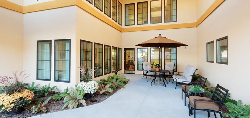 A cozy patio area with outdoor furniture and an umbrella, surrounded by large windows and decorative plants.