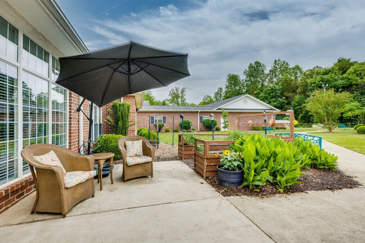 A cozy outdoor patio area with seating, an umbrella, and surrounding greenery.