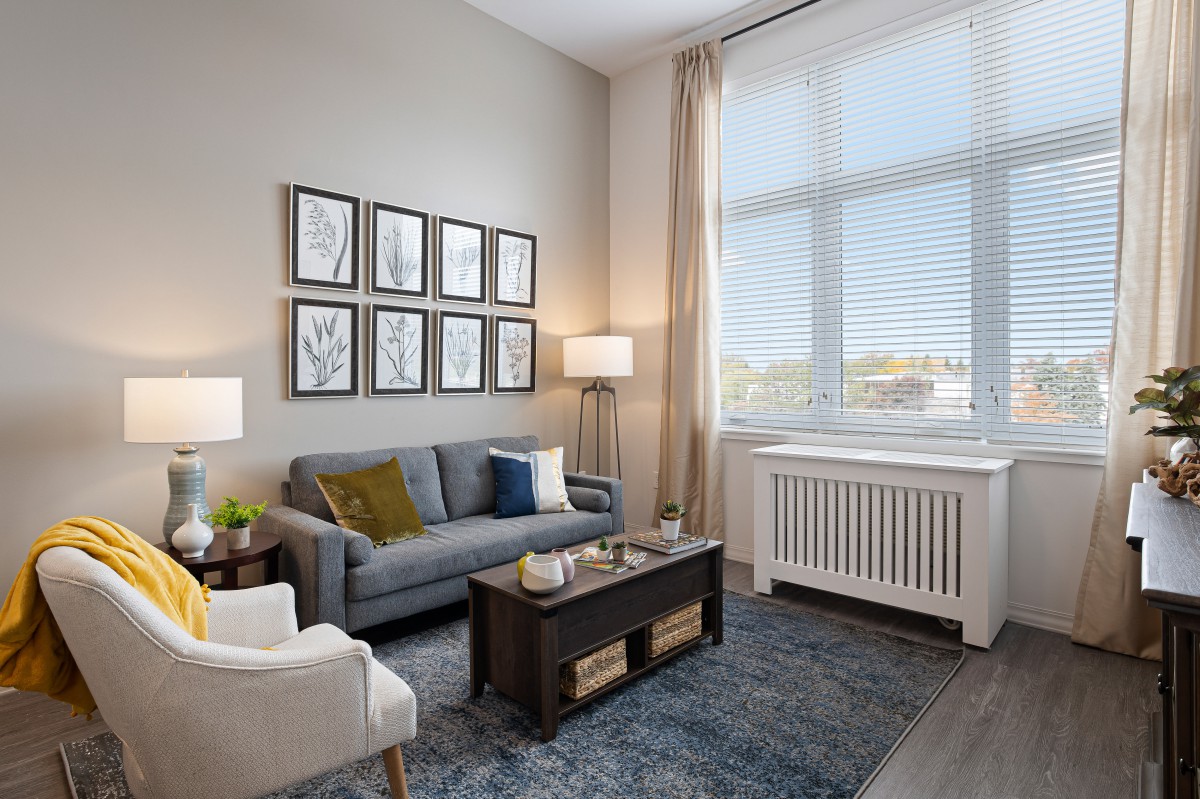 A cozy living room featuring a gray sofa, armchair, and a dark wooden coffee table with decorative items. The space is complemented by wall art and a large window with curtains.